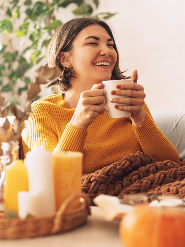 Lady drinks herbal tea brewed in a teapot in front of burning candles and a pumpkin